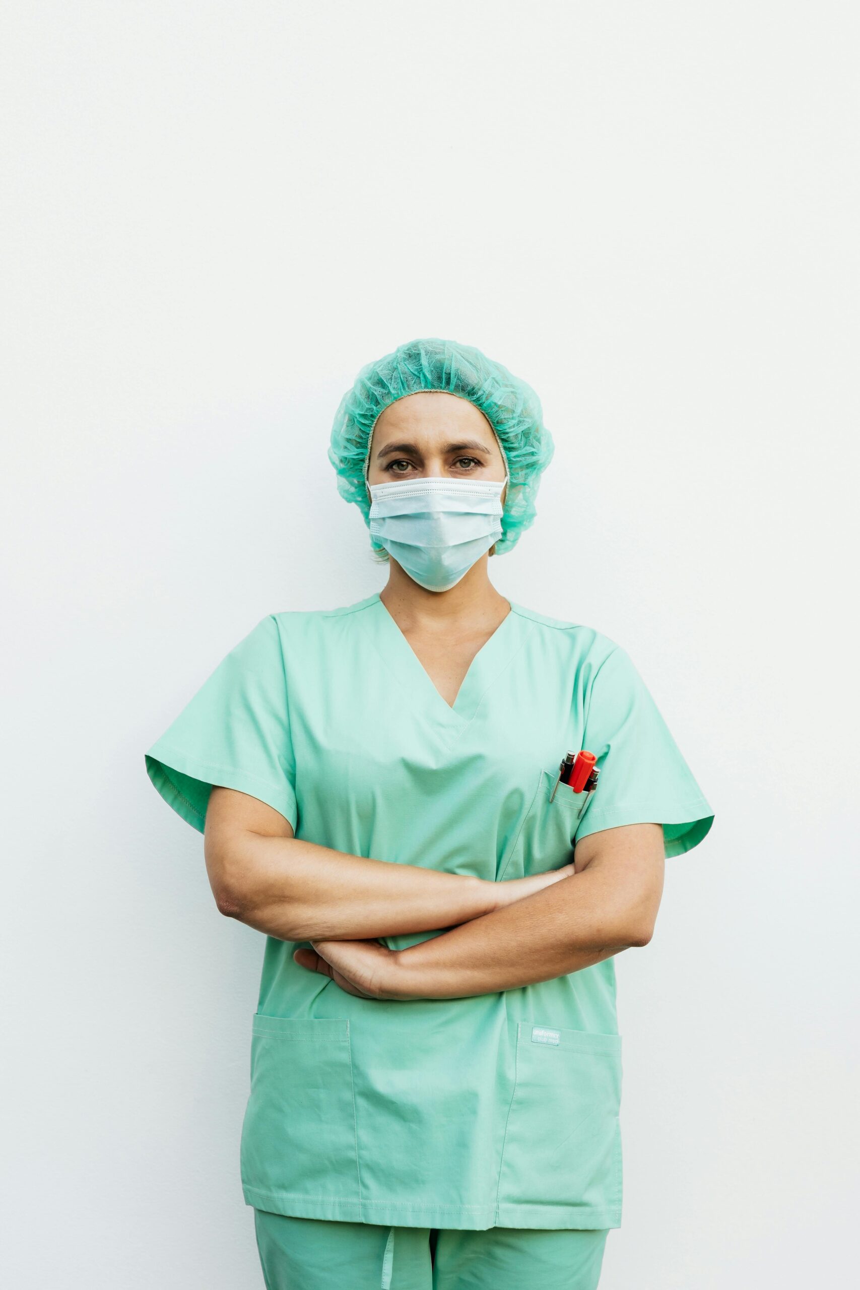 pexels-photo-5207087-5207087 A healthcare professional standing with arms crossed in green scrubs and a protective facemask.