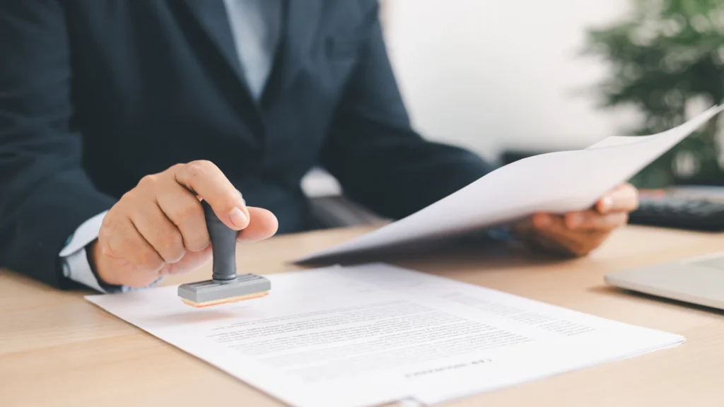 Close-up of a professional in a dark suit stamping an official document on a wooden desk.